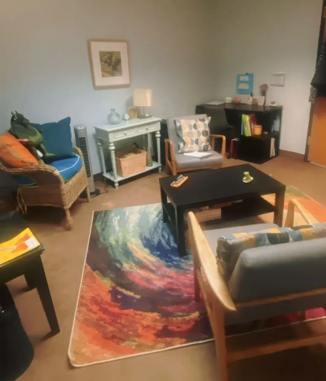 3 guest chairs in a office. The walls are light blue. There is a colorful carpet on the ground.