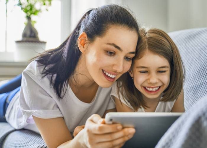 A woman and her daughter smile together while using a tablet