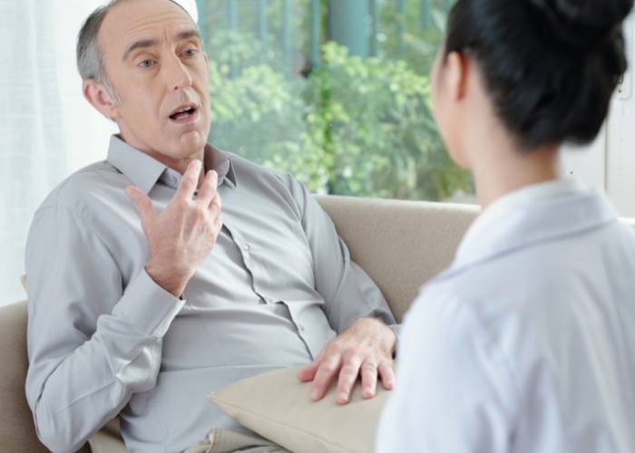 A man converses with a doctor while seated on a couch in a clinical setting